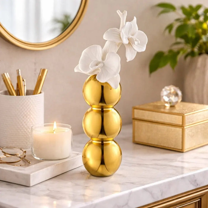 Gold stacked bubble flower diffuser by Waterdale Collection displayed on white surface with fresh white flowers and home decor accessories.
