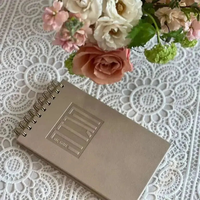 Tan leather Standing Haggadah by Waterdale Collection displayed on white lace with pink and cream roses nearby