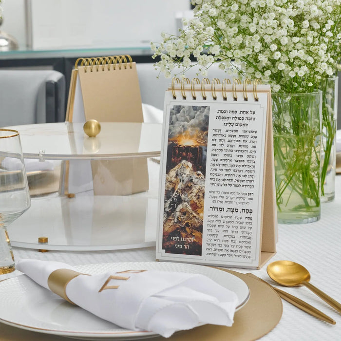 Standing leather Haggadah with painted details displayed next to a Passover place setting and gold spoon