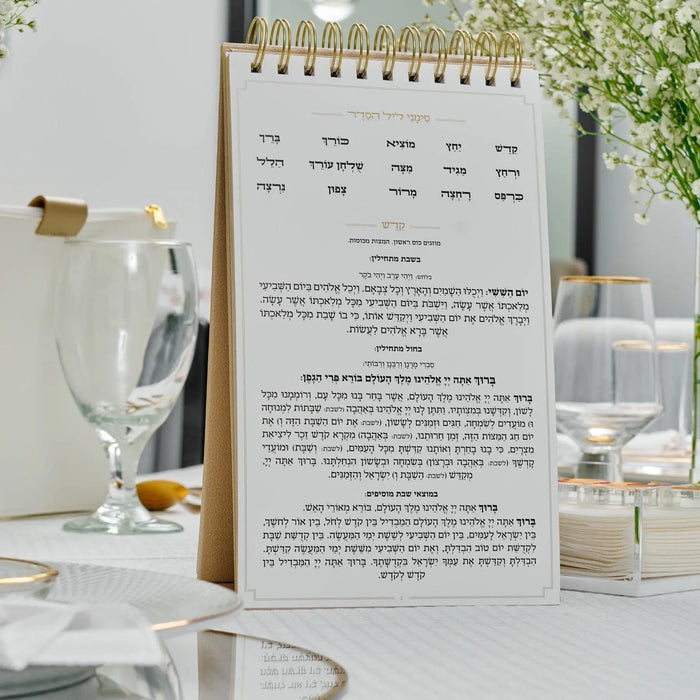 Standing leather Haggadah by Waterdale Collection displayed on white desk with wine glasses and Passover tabletop setting