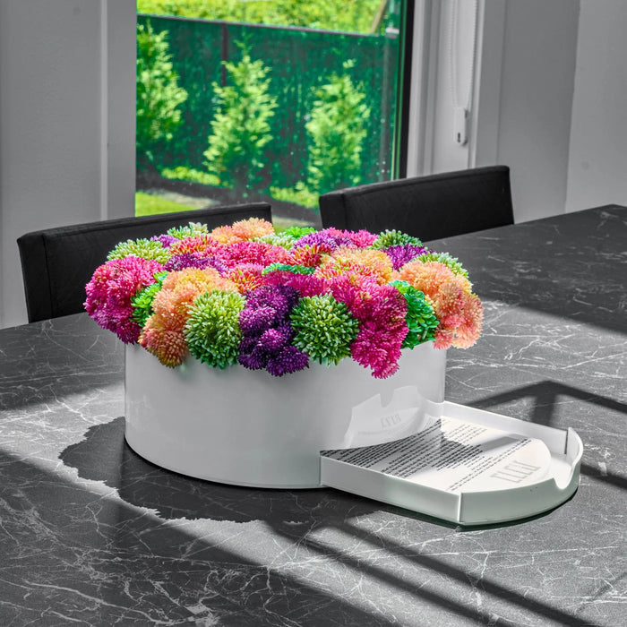 Pink and orange faux floral arrangement in white round vase on marble surface, modern home decor styling.