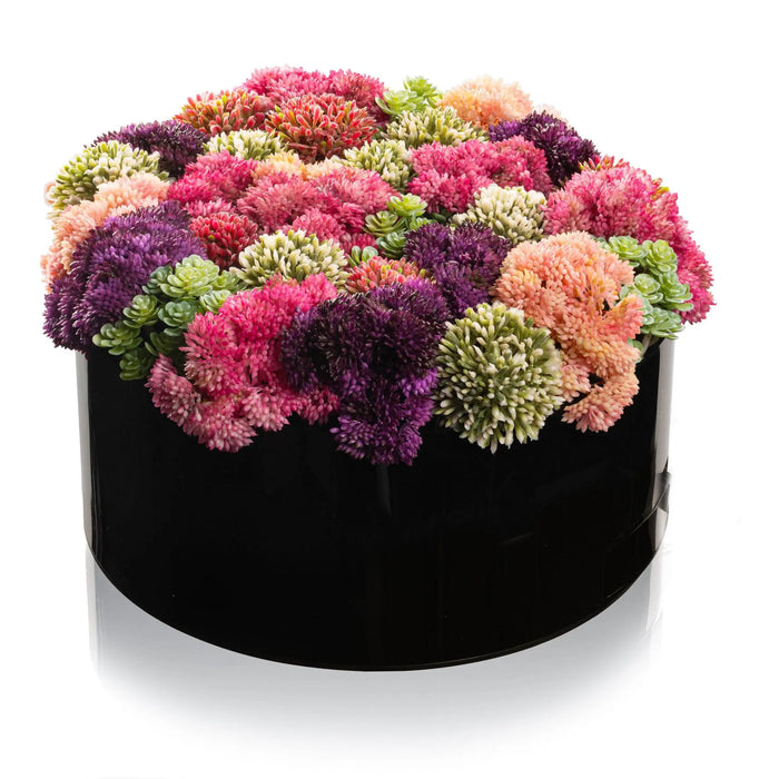 Pink and purple faux floral arrangement in a black round vase, featuring carnations and greenery for tabletop display.
