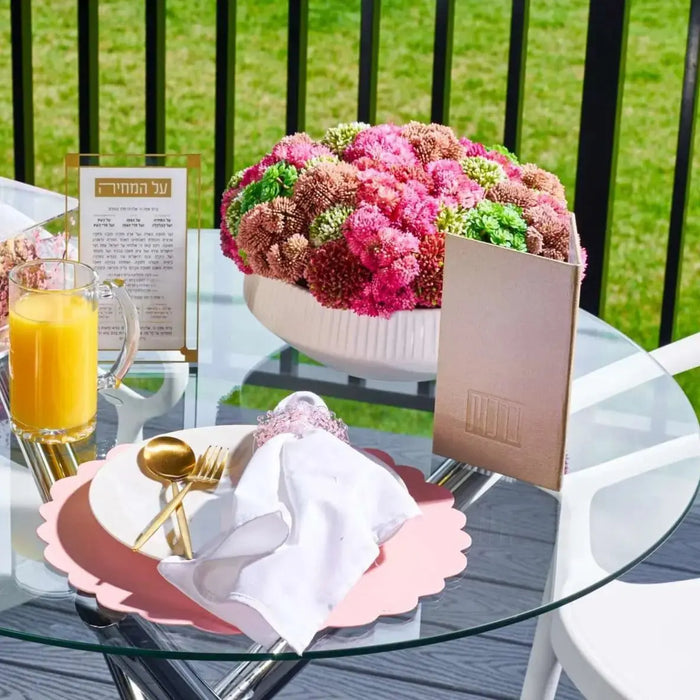 Pink and white succulent flower pot arrangement displayed on a black outdoor table with tableware and beverages in background