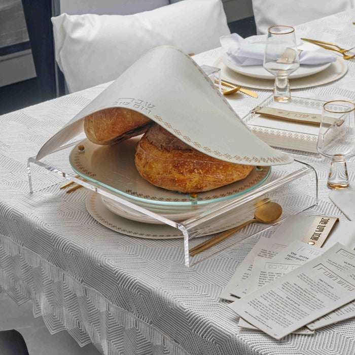 Marquesa Challah Cover in black leather with gold accents, displayed on a white table setting with place settings and bread during Shabbat dinner.