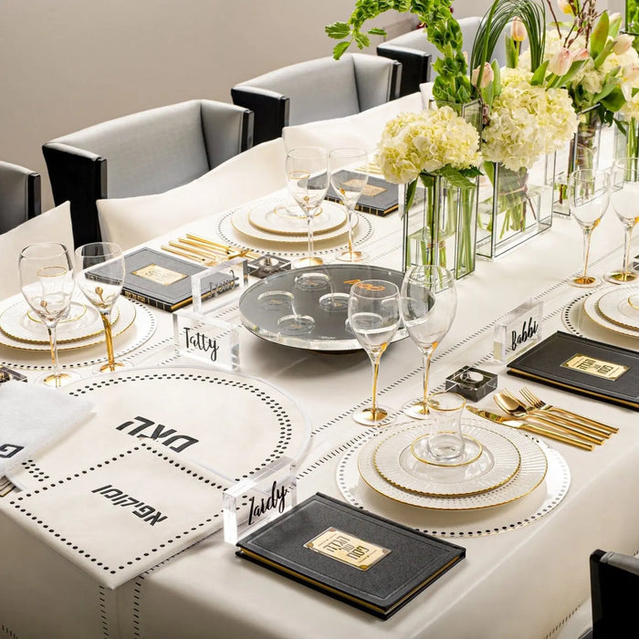 Cream leather tablecloth with hemstitch border displayed on dining table with place settings and flowers for Shabbat.