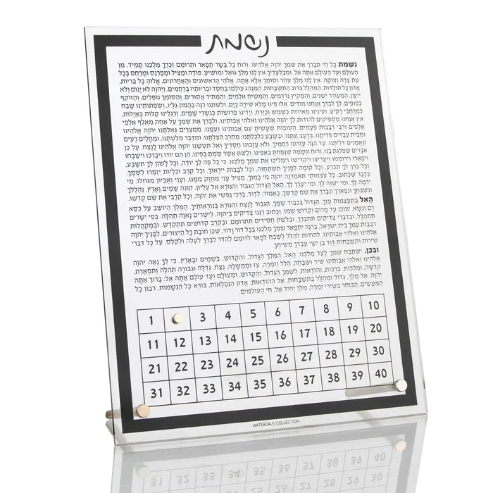 Tabletop Nishmas plaque with Hebrew text and calendar grid, black frame with white background, displayed at an angle on reflective surface.