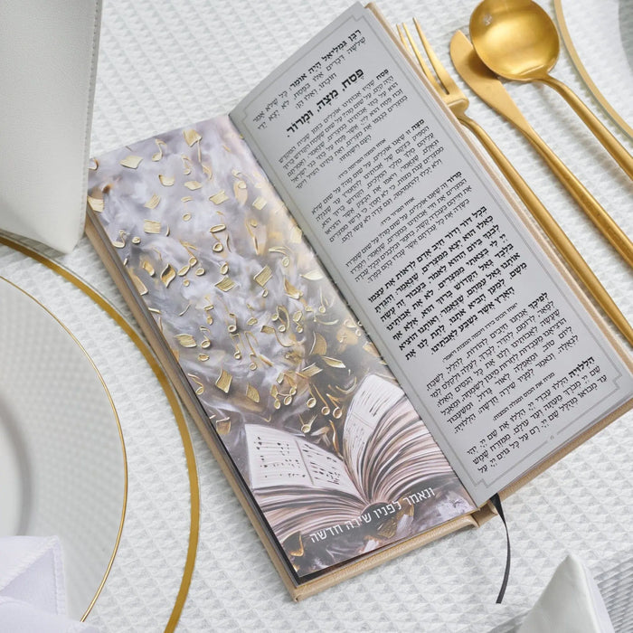 Tall leather painted Haggadah with floral design open on table, displayed with gold cutlery and white plate for Pesach