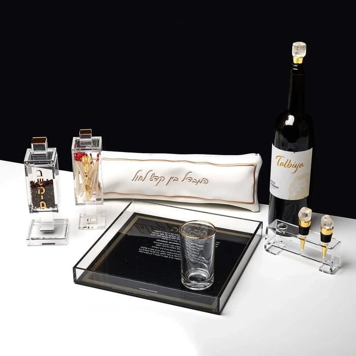 Black Havdalah plate with compartments for spices and wine, displayed with Shabbat candles and a bottle for traditional Jewish ceremony.