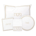 Trinket Pesach set with white leather placemats, napkin holder, plate charger, and coordinating gold-trimmed accessories arranged on white background.