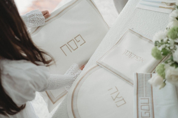 Trinket Pesach set in white leather with gold and silver accents, displayed with matching ceremonial items on a white surface.