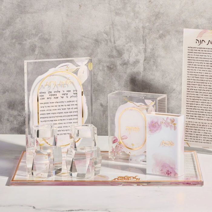 Watercolor Tzedakah Box with clear acrylic construction, gold accents, pink floral details, displayed on matching tray with Hebrew text card and coordinating candles.
