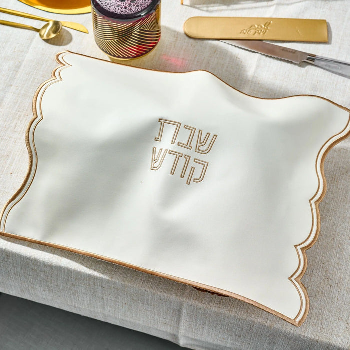 White Wave Edge Challah Cover with gold trim and embroidered Hebrew text, displayed on table with Shabbat items