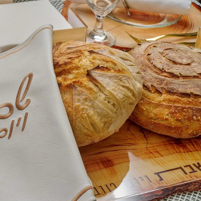 Wooden Challah board with carved handles displayed with fresh baked challah bread and wine glass on table setting for Shabbat.