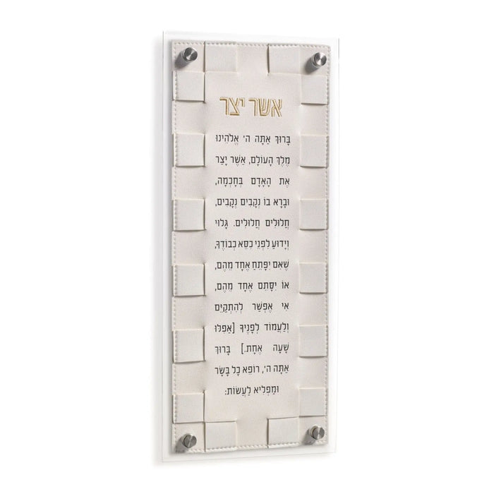 Woven Asher Yatzar wall art in cream with Hebrew text and textured brick-pattern background, mounted with metal corners.
