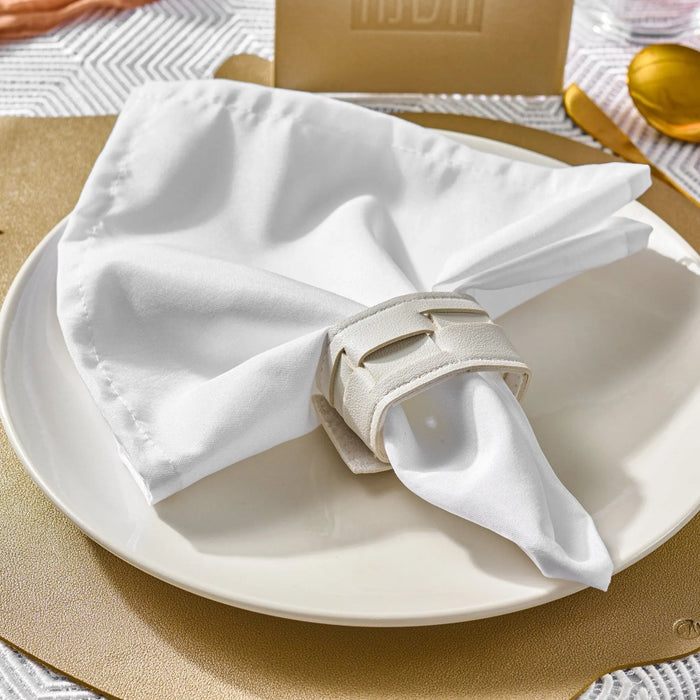 Woven leather napkin wrap in silver holding a white cloth napkin on a plate with place setting and gold accents.