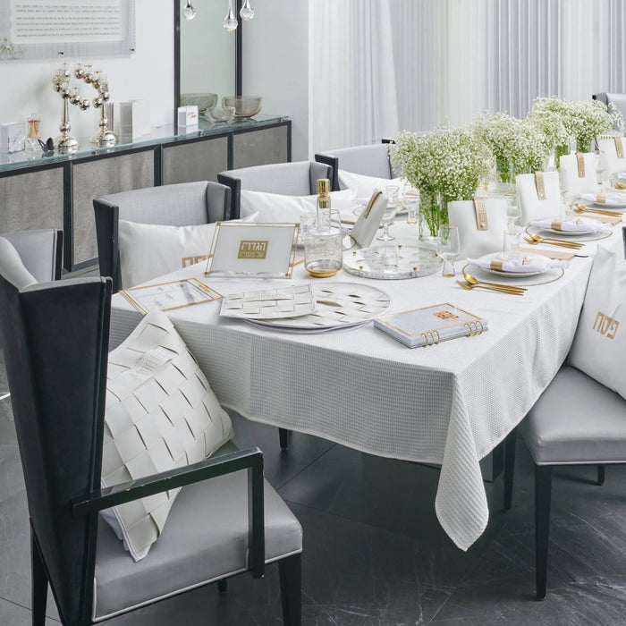 Woven Leather Pesach Set in gold and white displayed on a formal dining table with place settings and white linens.
