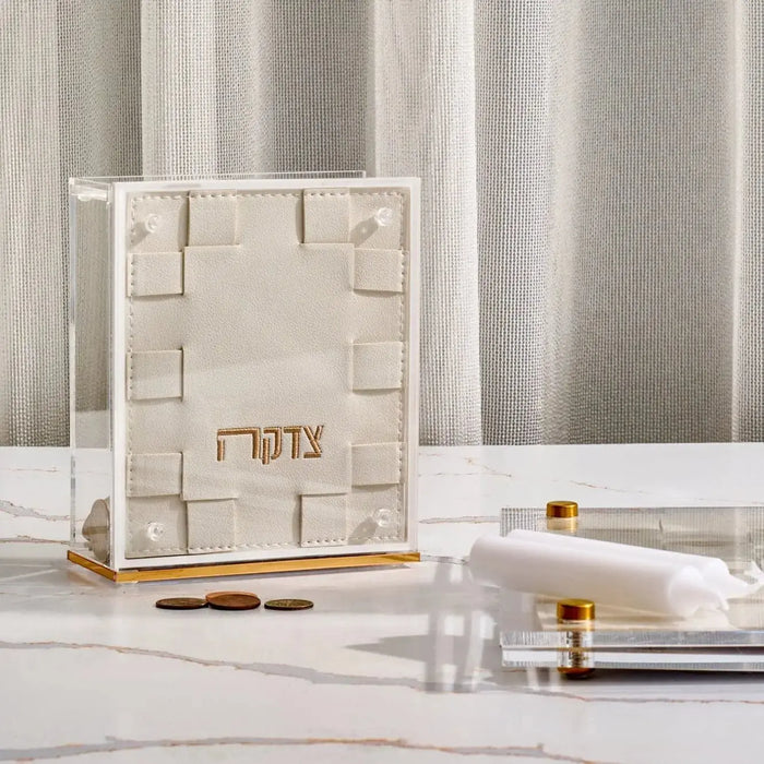 Cream woven tzedakah box with geometric cutout patterns displayed on white surface with candles and matches nearby.